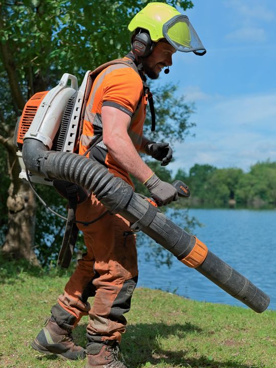 Quill Hall operator using a backpack blower to clear arisings beside a lake