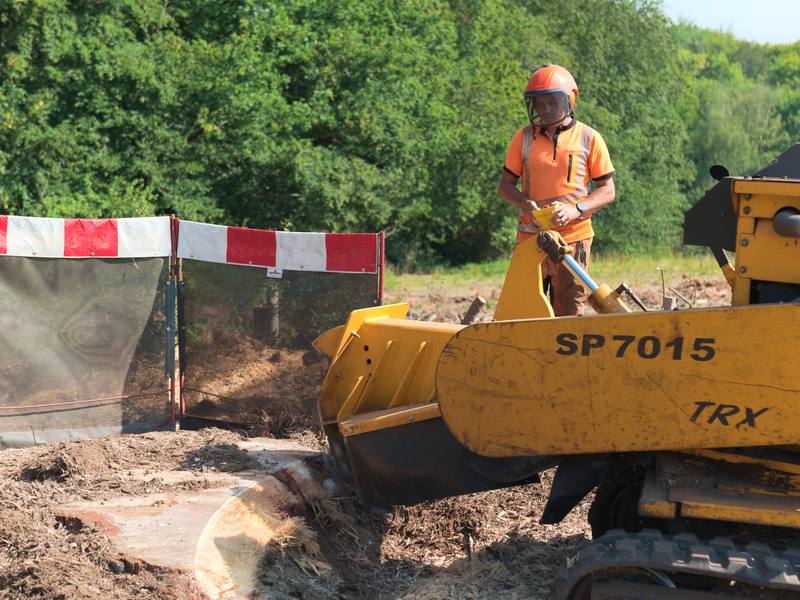 Operator running a tracked stump grinder that is throwing up grindings